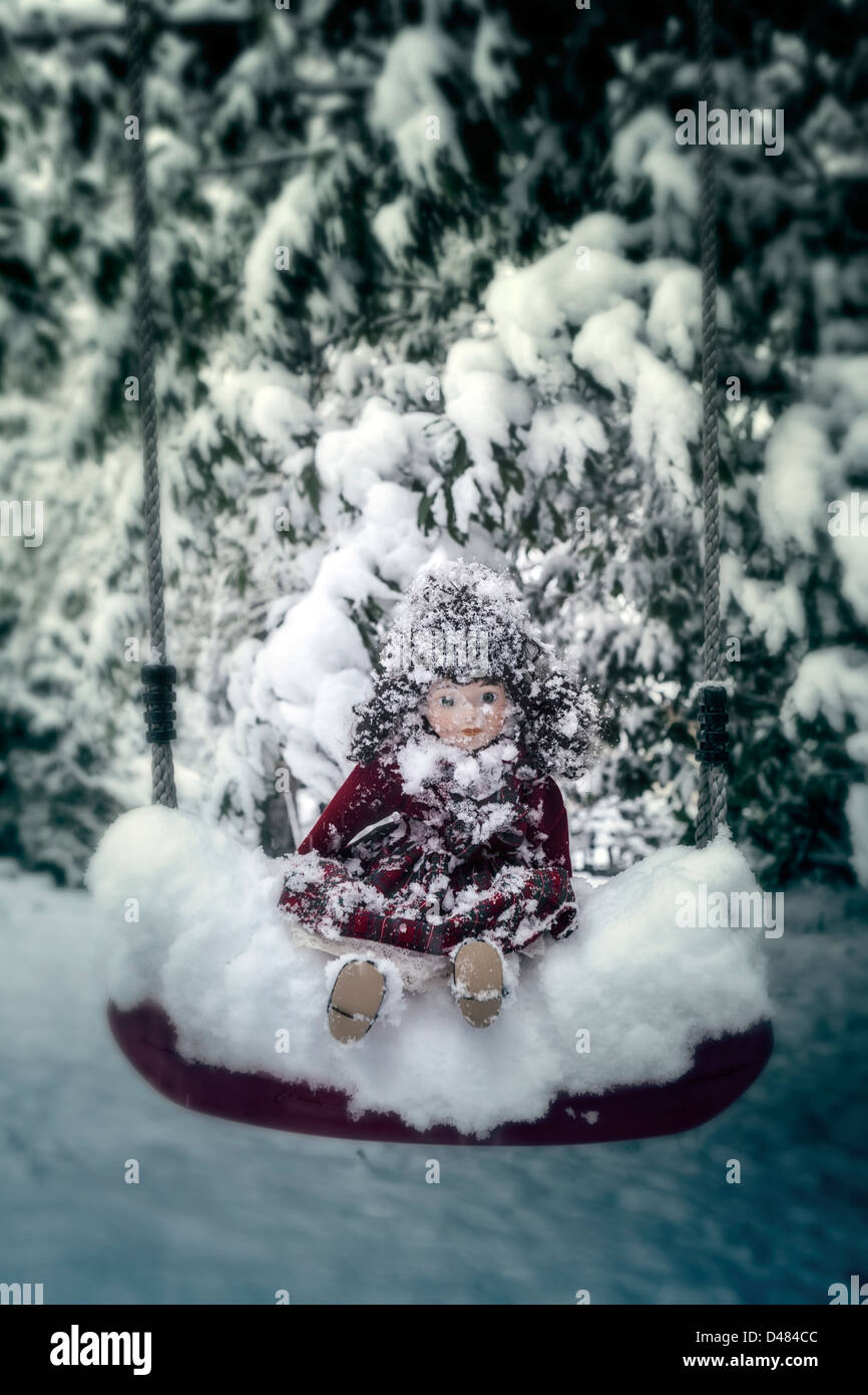 a snow-covered doll sitting on a swing Stock Photo