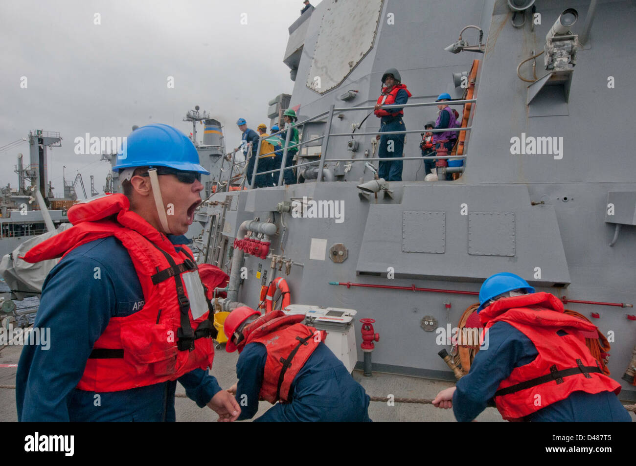 Sailor directs line handlers at sea Stock Photo Alamy