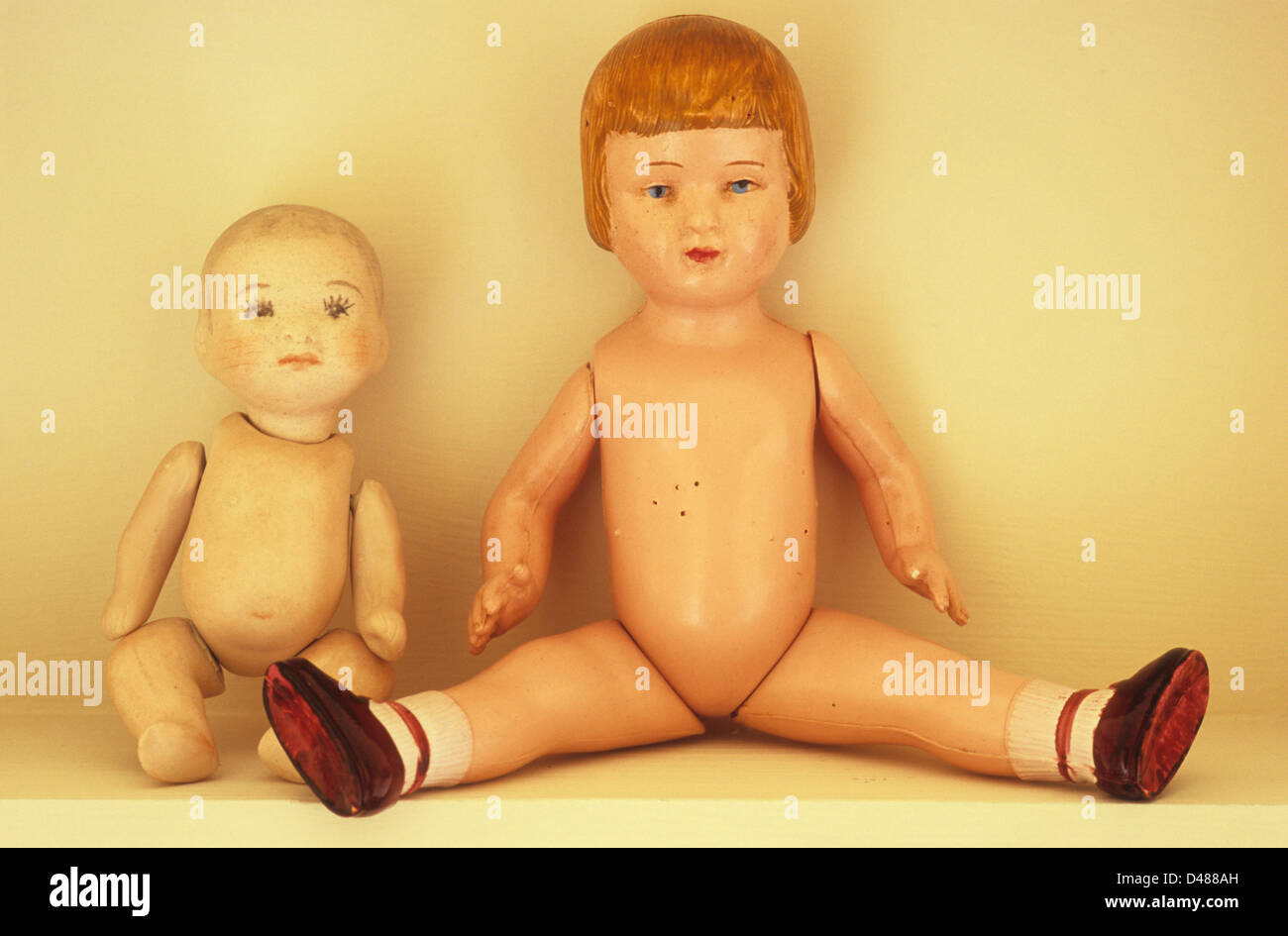 Traditional bisque baby girl doll sitting on shelf next to vintage celluloid girl doll with legs open Stock Photo