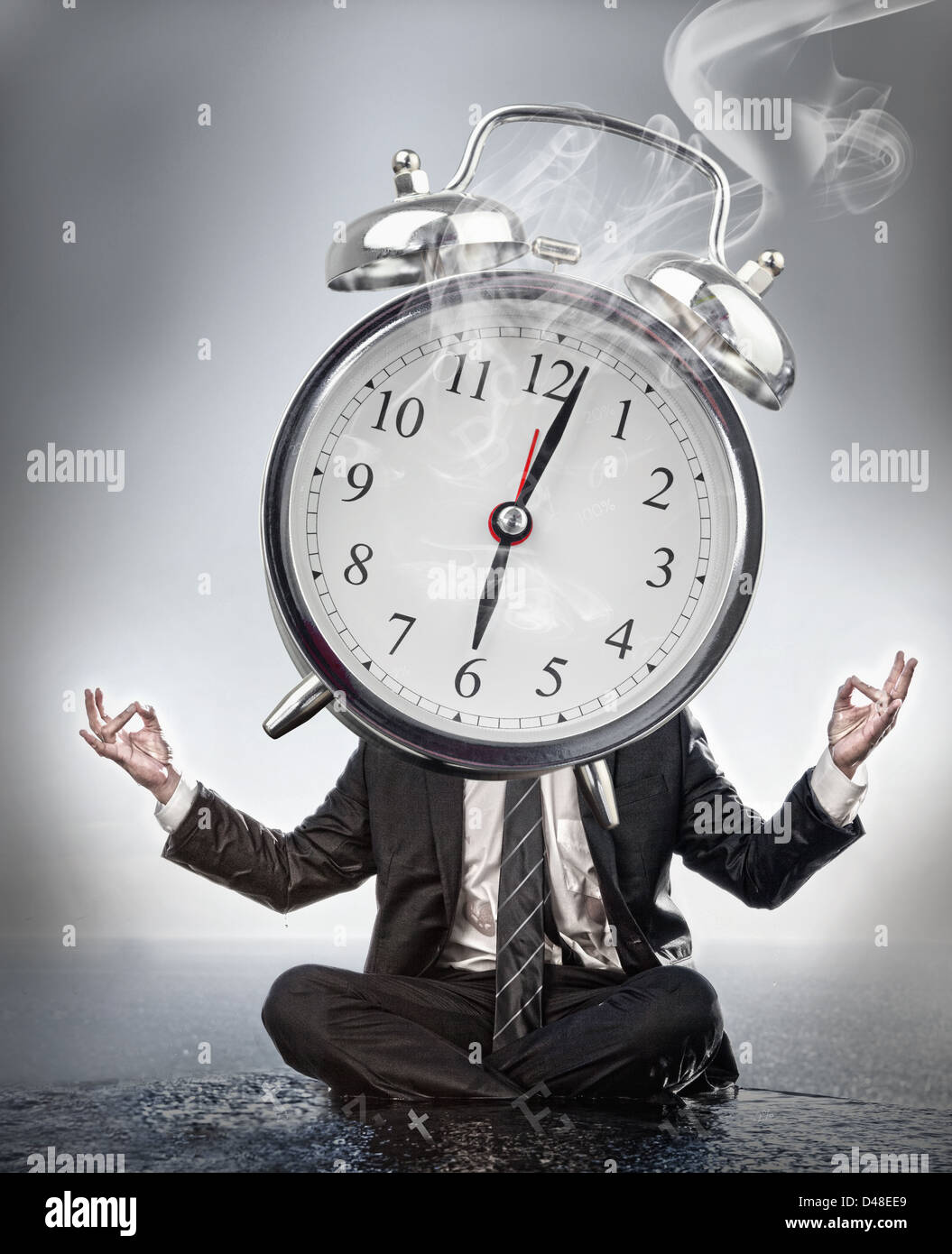 Businessman meditating with face covered by alarm clock Stock Photo
