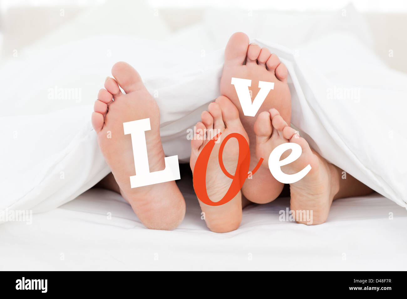 Pair of feet under duvet with love text Stock Photo
