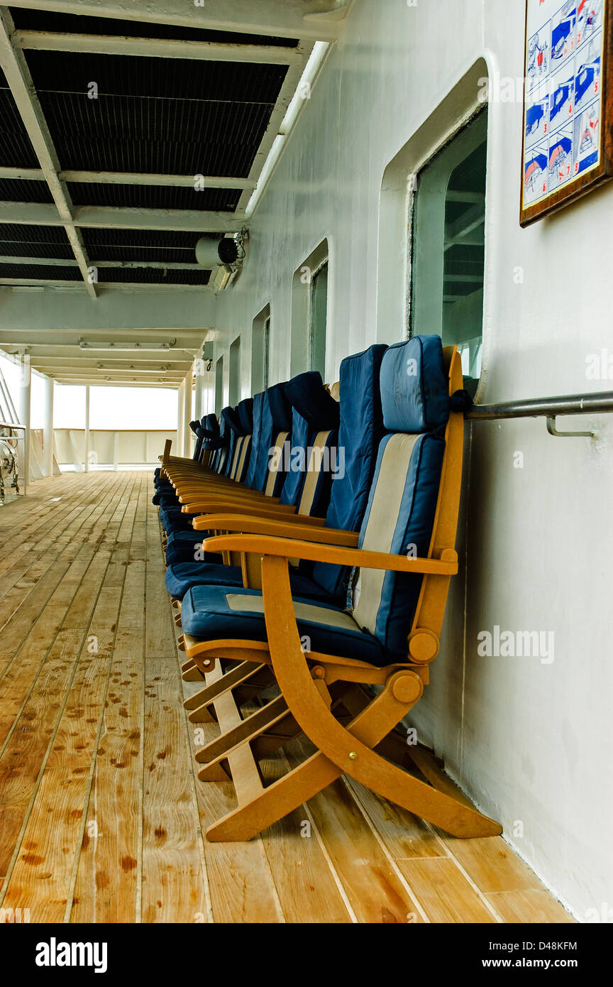 Blue and grey padded seats stand empty on freshly scrubbed deck boards as the ship sails through mist towards Southampton Stock Photo