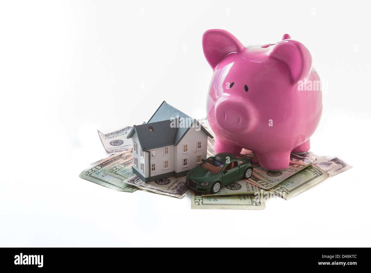 Piggy bank toy car and miniature home resting on pile of dollars Stock Photo