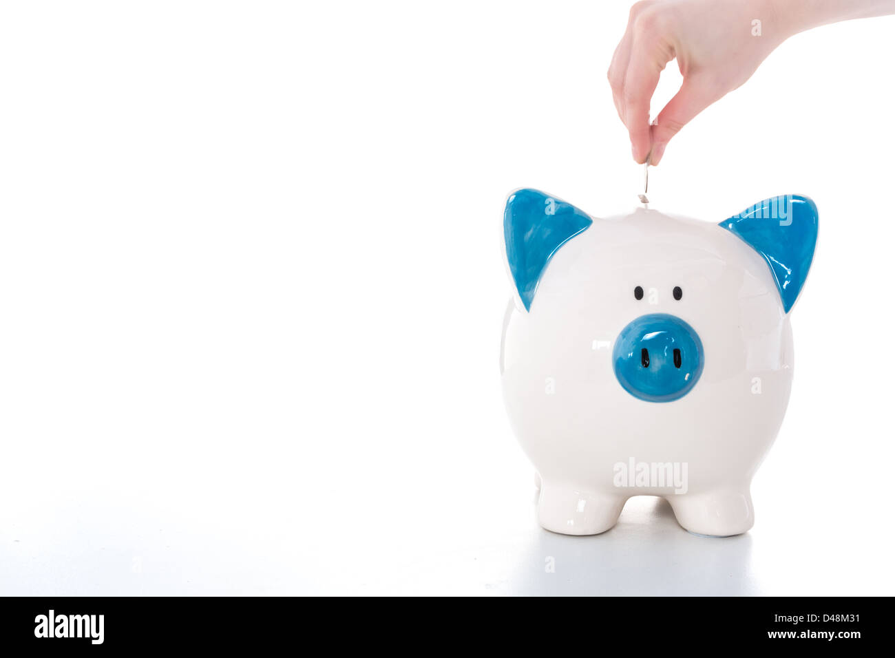 Hand putting coin into blue and white piggy bank Stock Photo - Alamy
