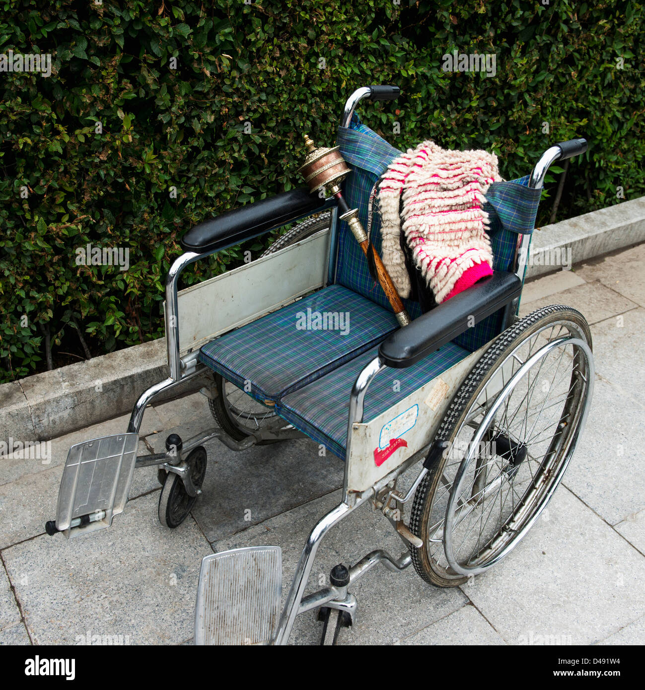 A wheelchair sits on a sidewalk with a blanket and traditional chinese item;Lhasa xizang china Stock Photo