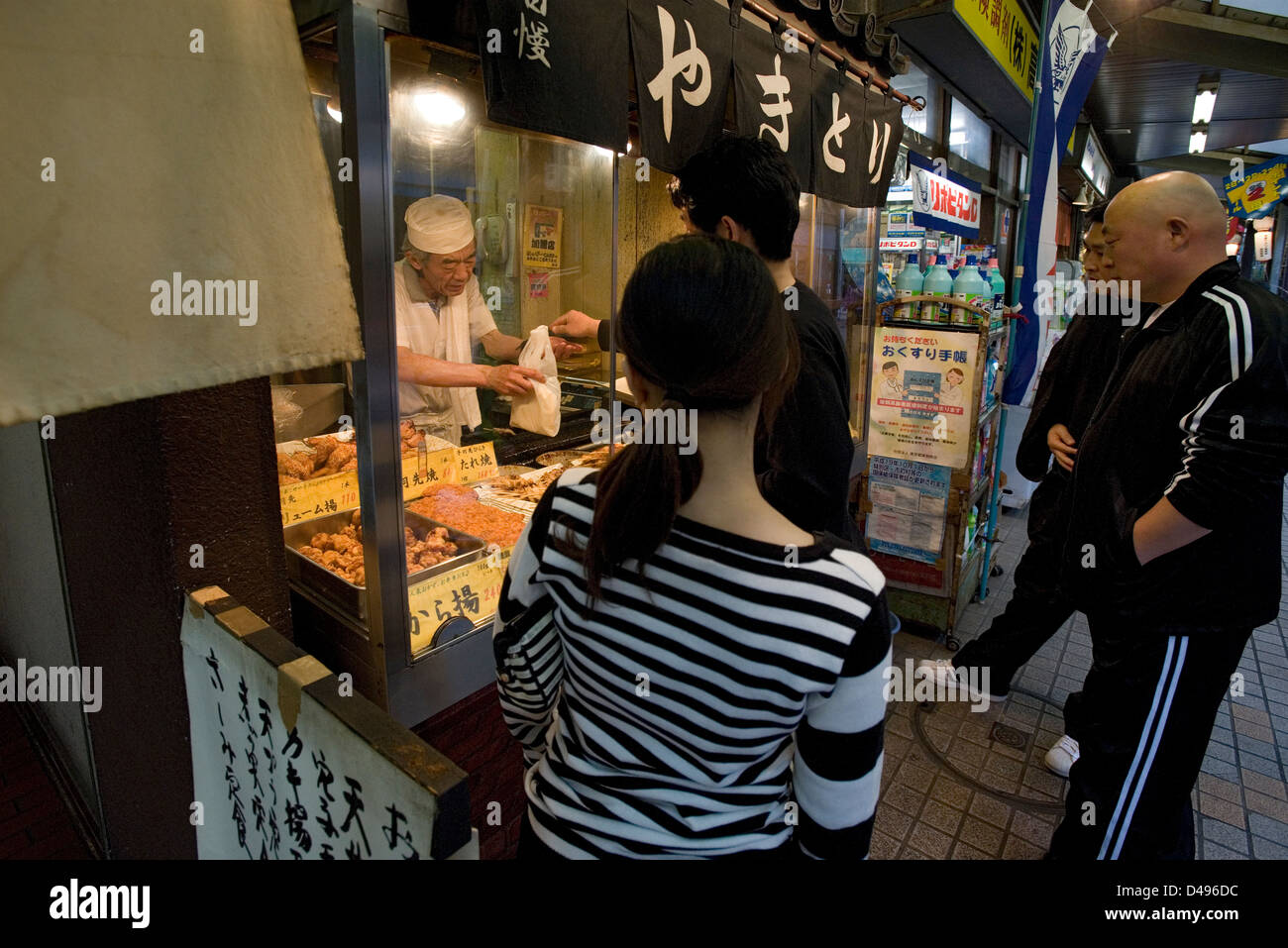 Customers line up for some delicious yakitori, chicken on skewers, at a little sidewalk shop in the Tsukishima, Tokyo. Stock Photo