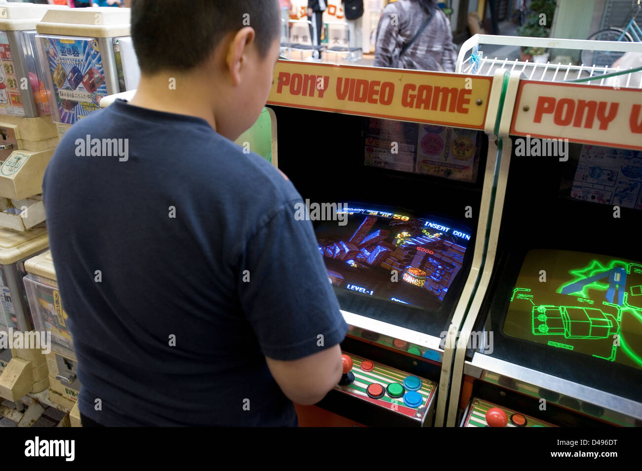 A young boy playing an old-fashioned pony video game on a sidewalk arcade in Akihabara, Tokyo. Stock Photo