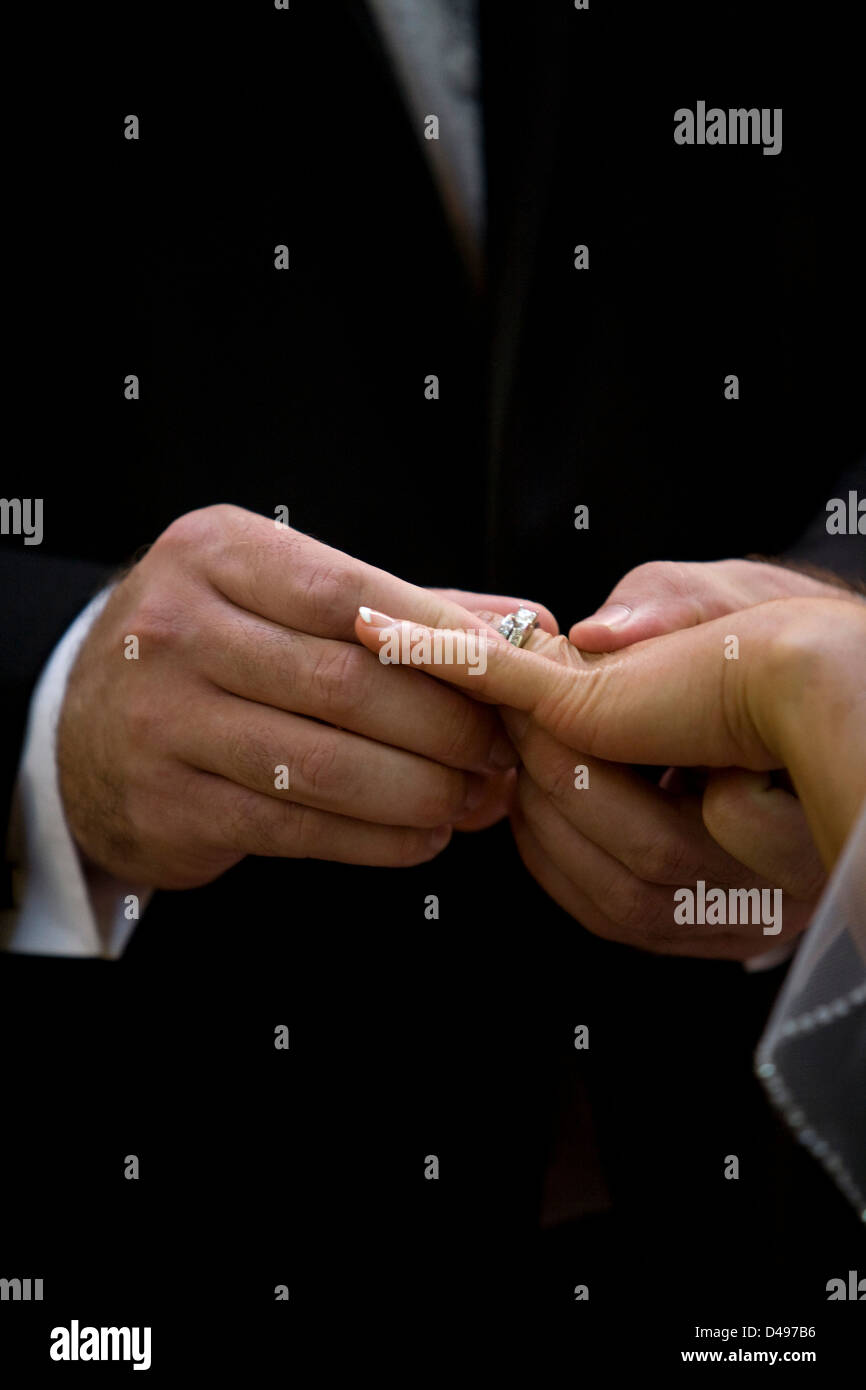 A groom places a ring onto his brides finger during a wedding ceremony ...
