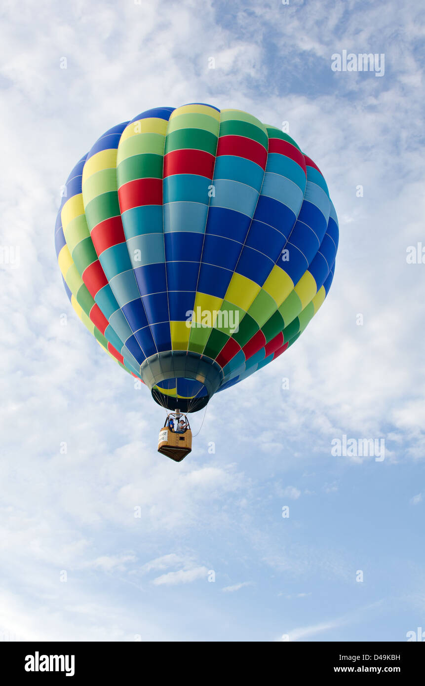 A rainbowcolored hot air balloon floats through white clouds in a blue
