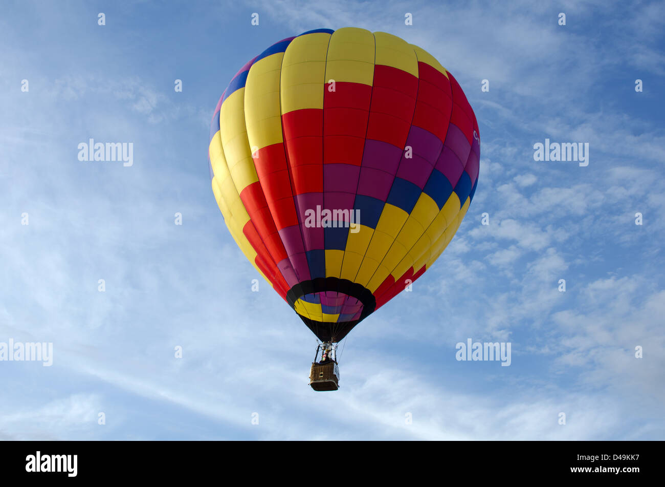 A hot air balloon floats overhead into a blue sky streaked with wispy ...