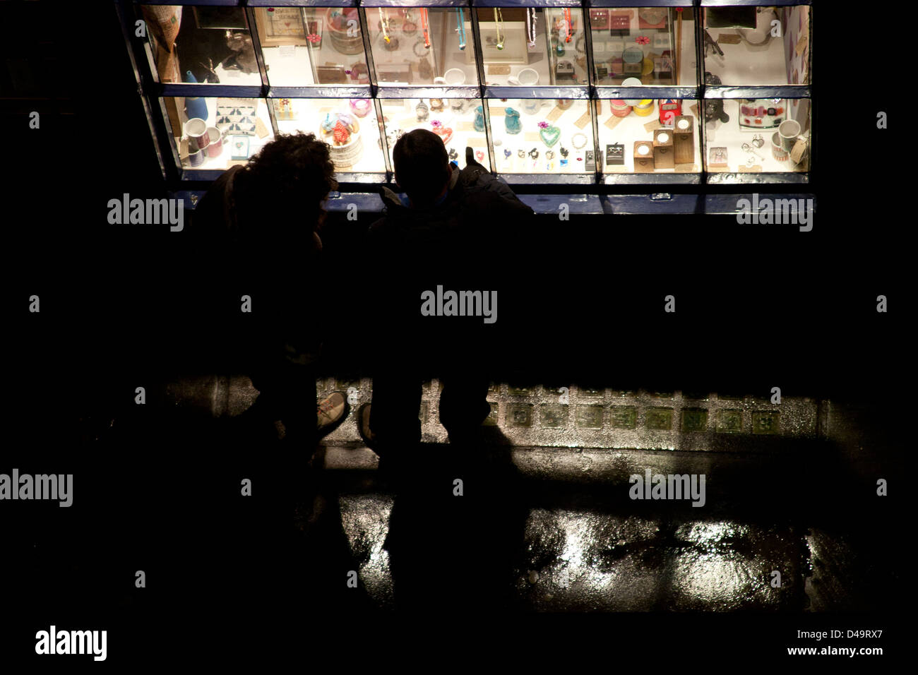 Two people looking in a brightly lit shop window at night High Petergate, York, Yorkshire England UK Stock Photo