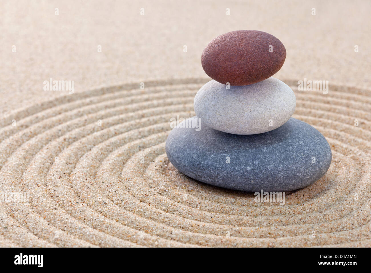 Three pebbles stacked on a circular raked zen garden Stock Photo