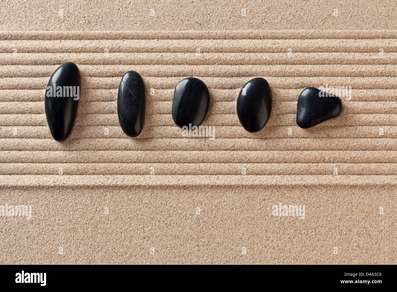 Five black pebbles on a raked sand zen garden. Stock Photo