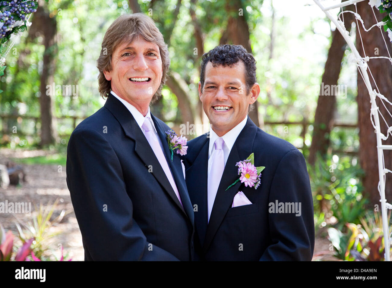 Handsome gay couple getting married under a floral archway, in outdoor ceremony.  Stock Photo