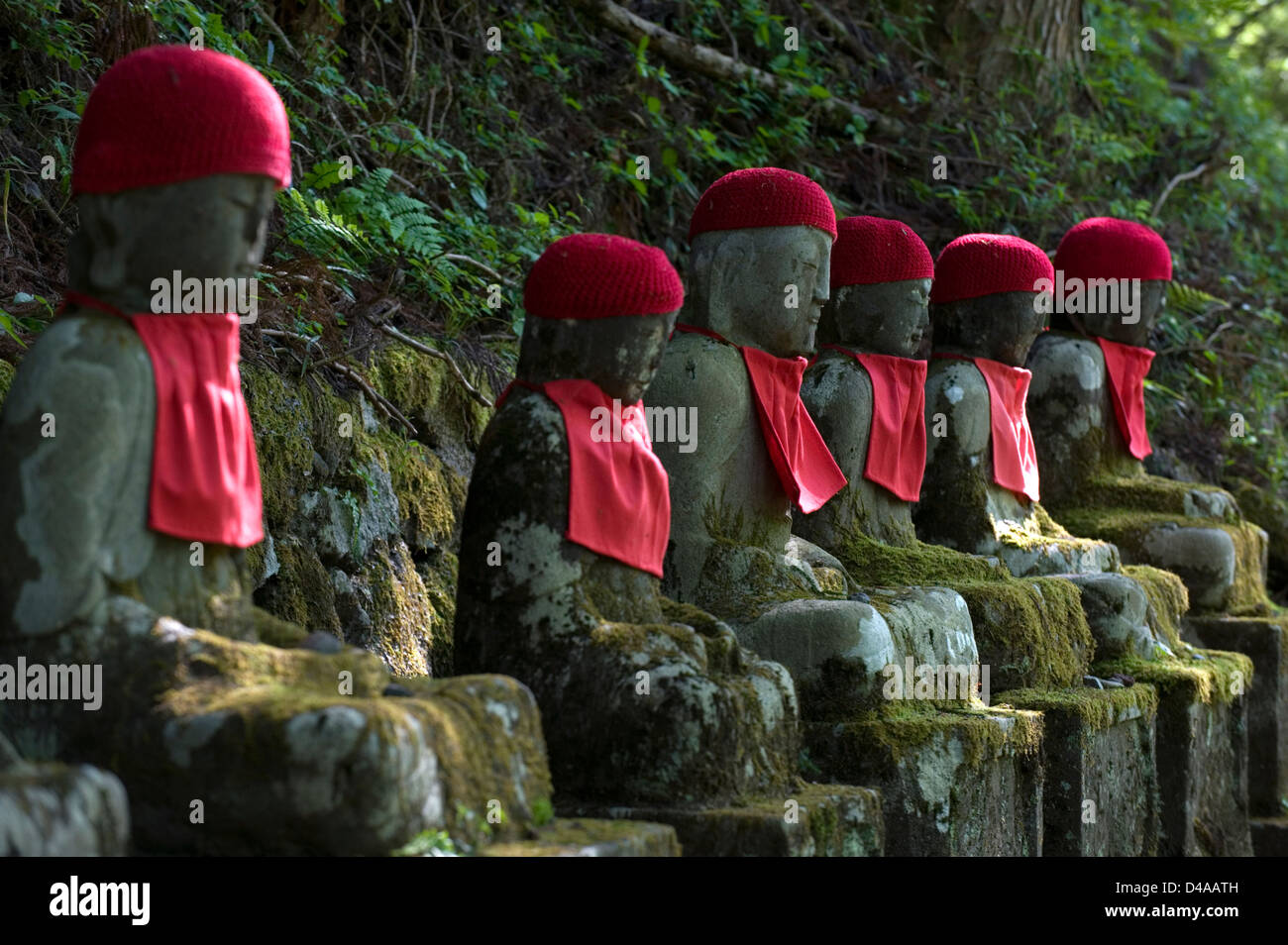 Row of stone 'jizo' sitting Buddha statues with red bibs and caps in the Ganmangafuchi Abyss forest of Nikko, Tochigi, Japan. Stock Photo