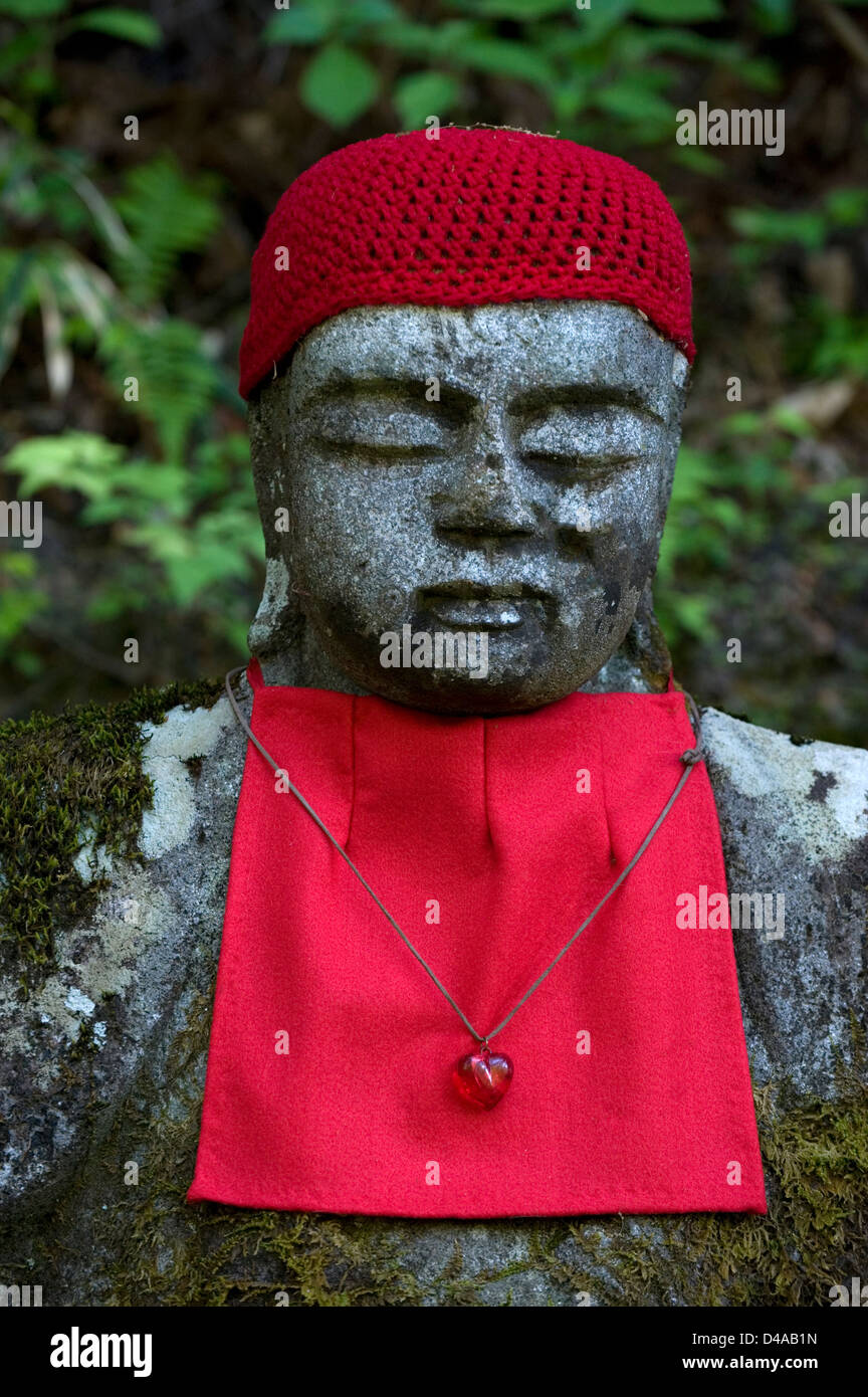 Stone 'jizo' sitting Buddha statue with red bib and cap and heart-shaped charm around his neck in the Ganmangafuchi Abyss Stock Photo