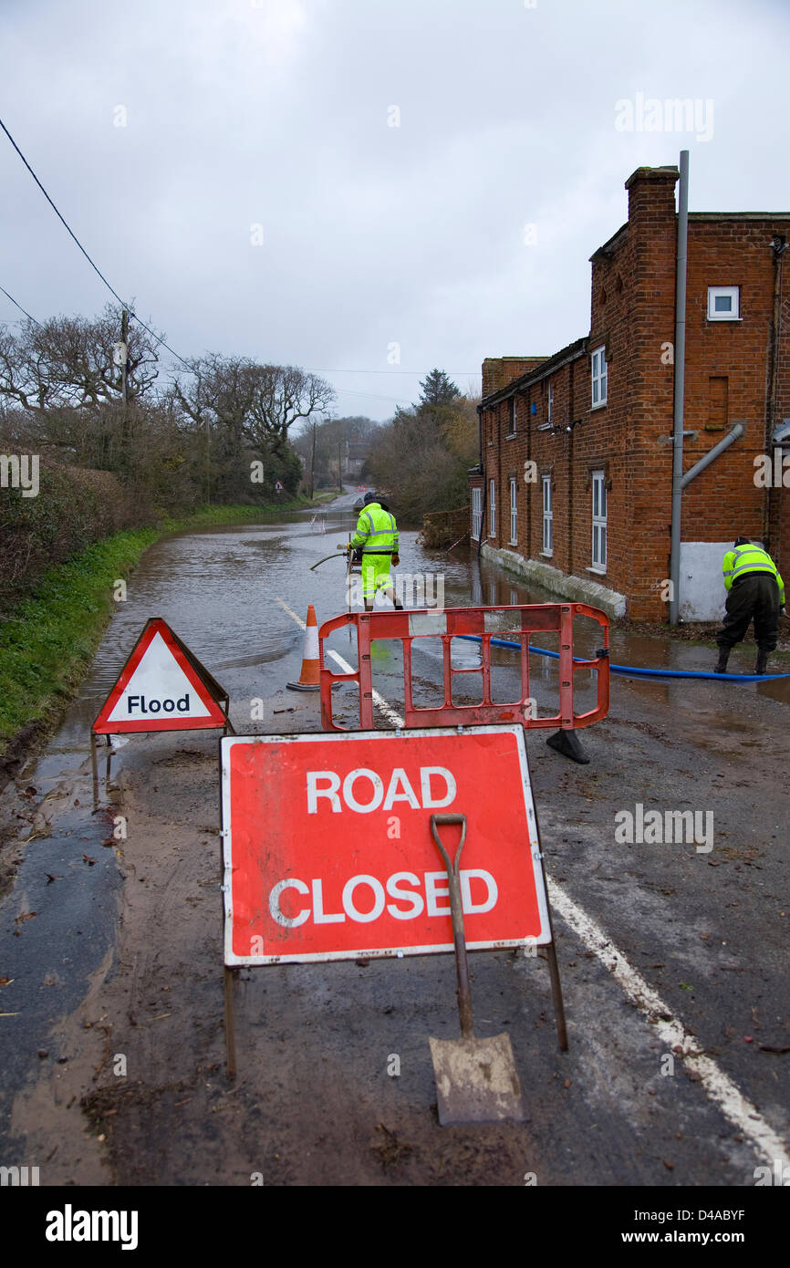 A UK road closed because of flooding due to heavy rainfall. Road closed  sign, Flood sign and orange barriers. Workmen work to try & clear the flood waters with water pumps. Stock Photo