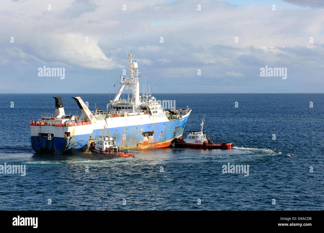 An ocean going fishing boat being manouvered by two tug boats in the  Strait of Magellan .  Punta Arenas, Chile. Stock Photo