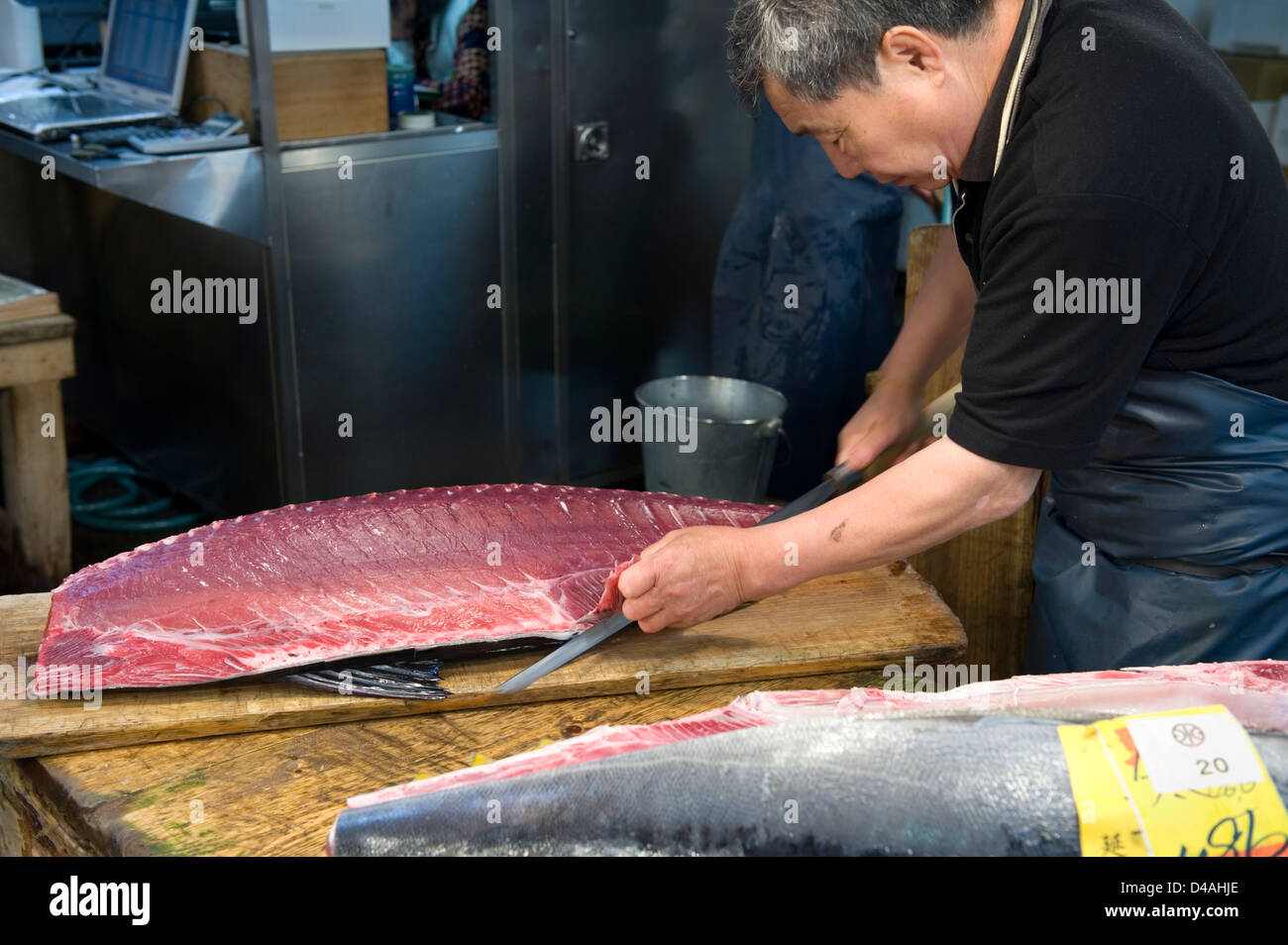 A fishmonger slices up a large fresh tuna with a sharp knife at Tsukiji