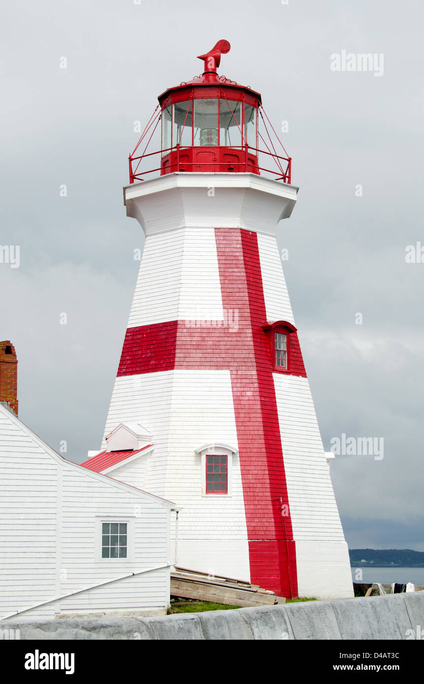 The red-and-white painted East Quoddy Lighthouse gleams in a ray of sun against a stormy gray sky. Stock Photo