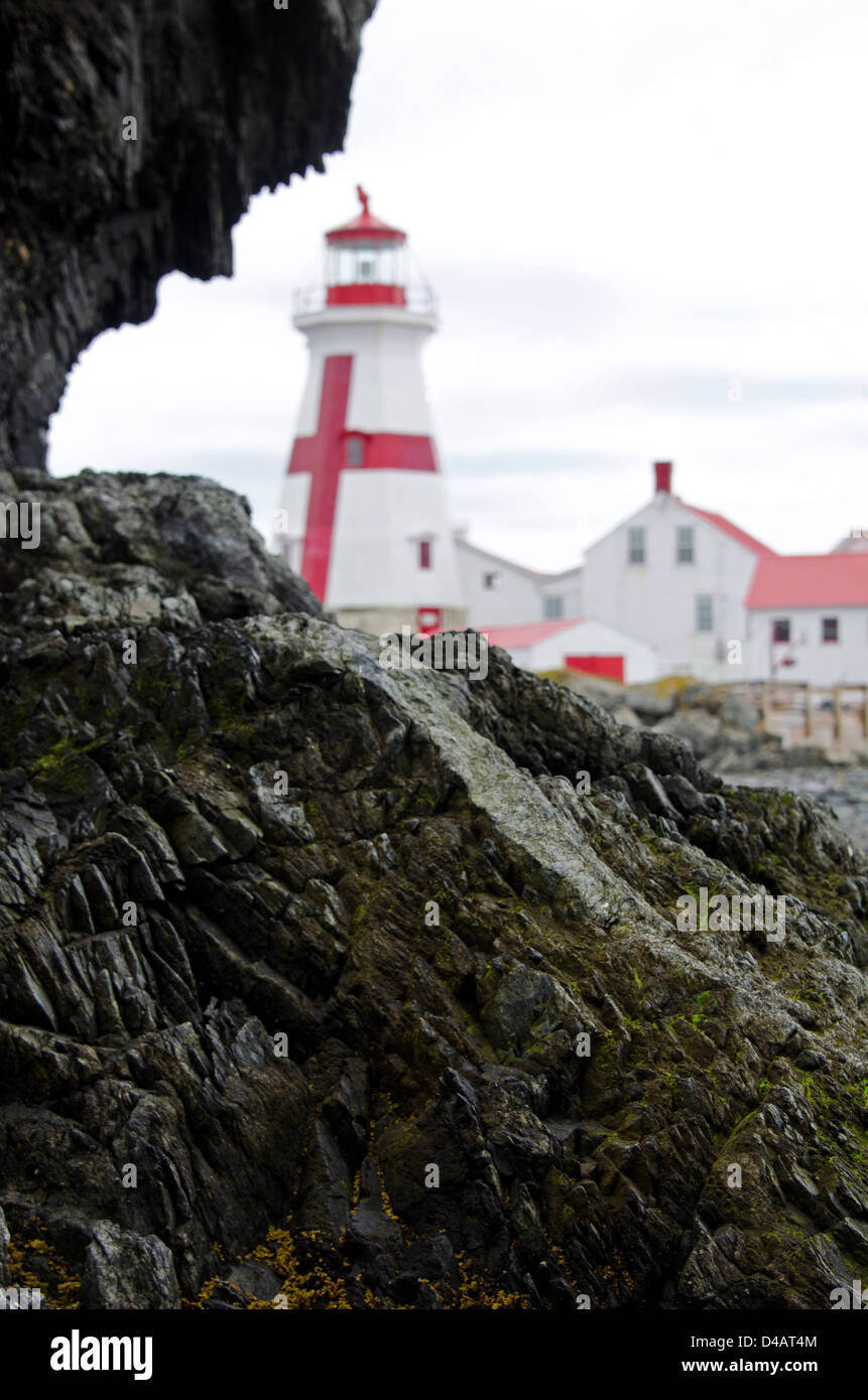A dark rock outcrop frames the East Quoddy Lighthouse (also known as the Head Harbor Light.) Stock Photo