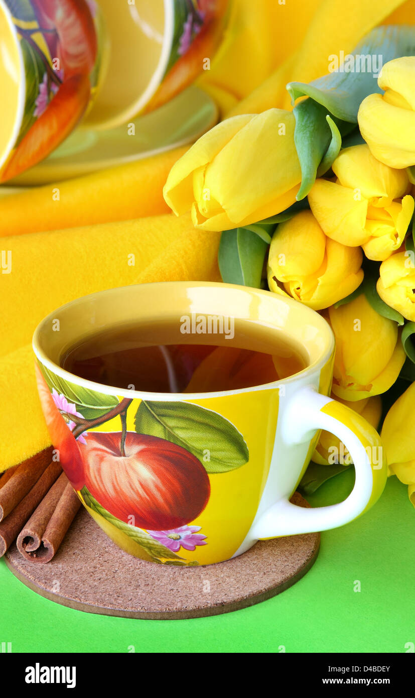 Tea cups and yellow tulips on green background Stock Photo