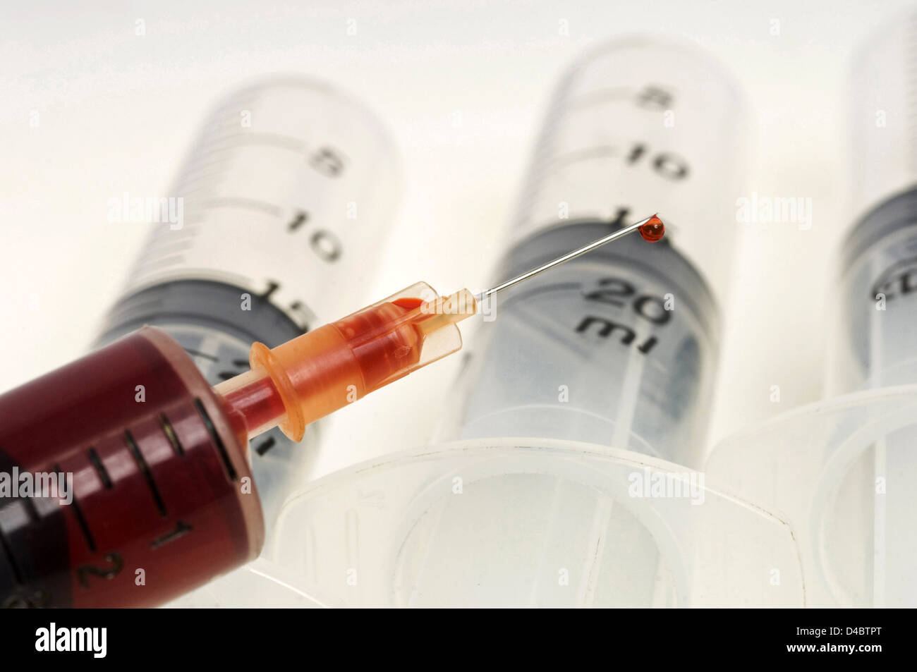 Close up of needle with droplet of liquid attached to syringe in front