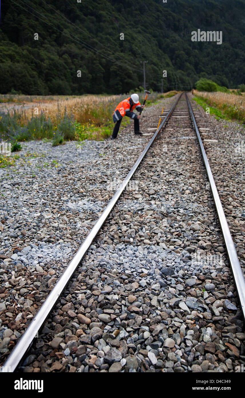 A man wearing high visibility jacket and hard hat using a sledgehammer working on a single track railway line. Stock Photo