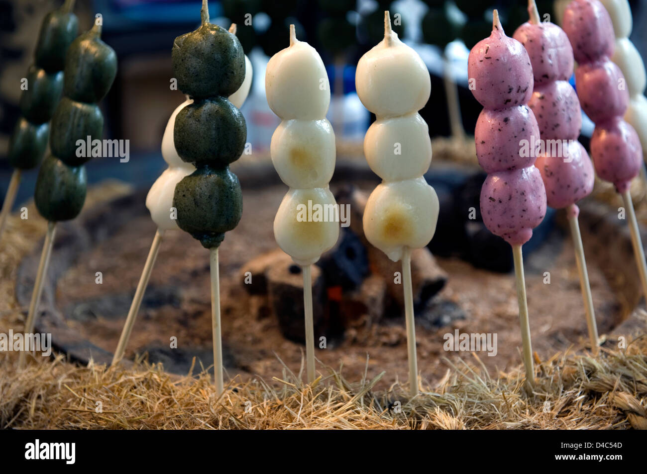 Green, white and pink 'dango' (three mochi rice cake balls on a skewer), Japanese treats being warmed over glowing hot coals. Stock Photo