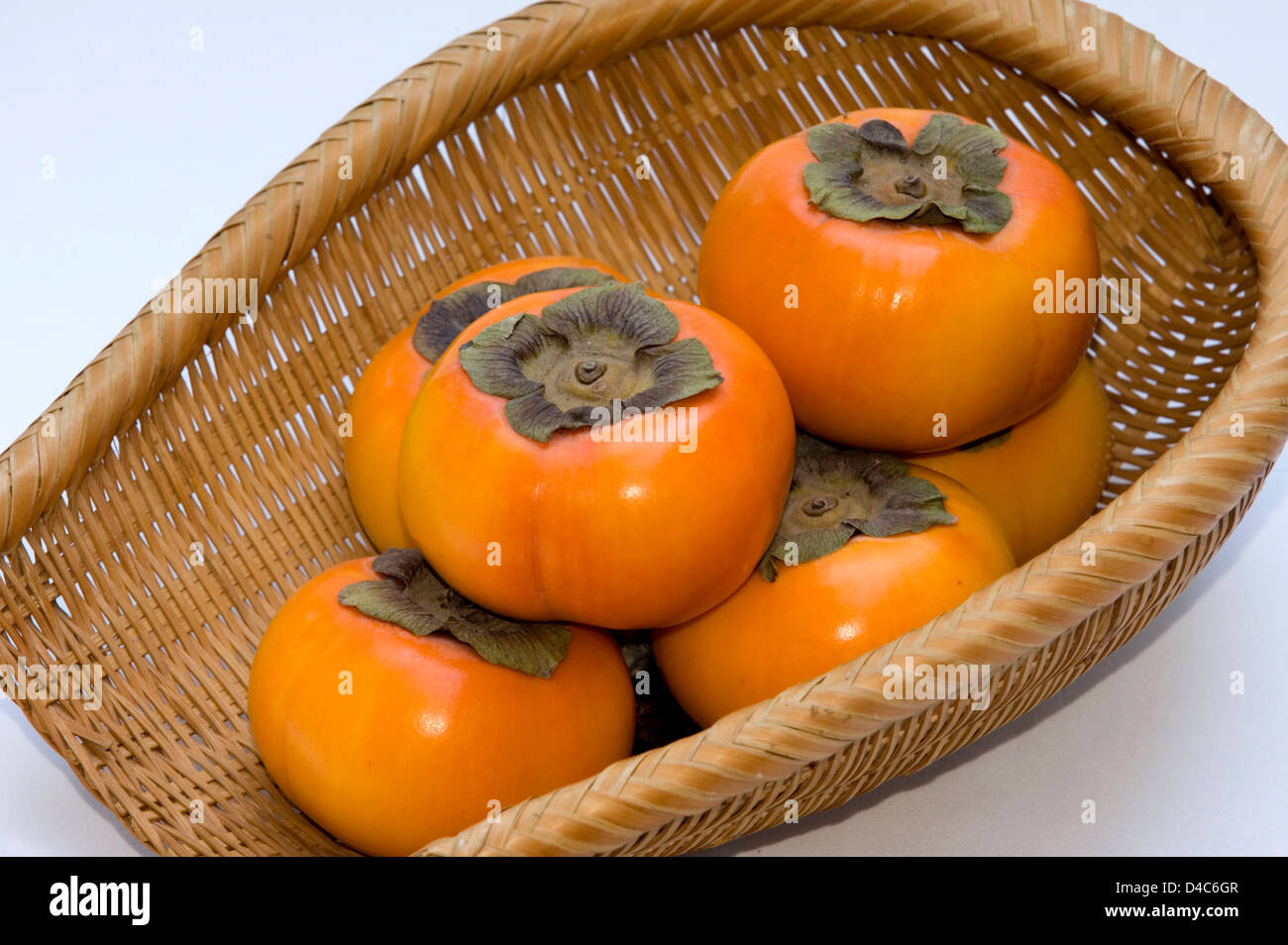A wicker basket containing fresh Japanese 'kaki' persimmon fruit. Stock Photo