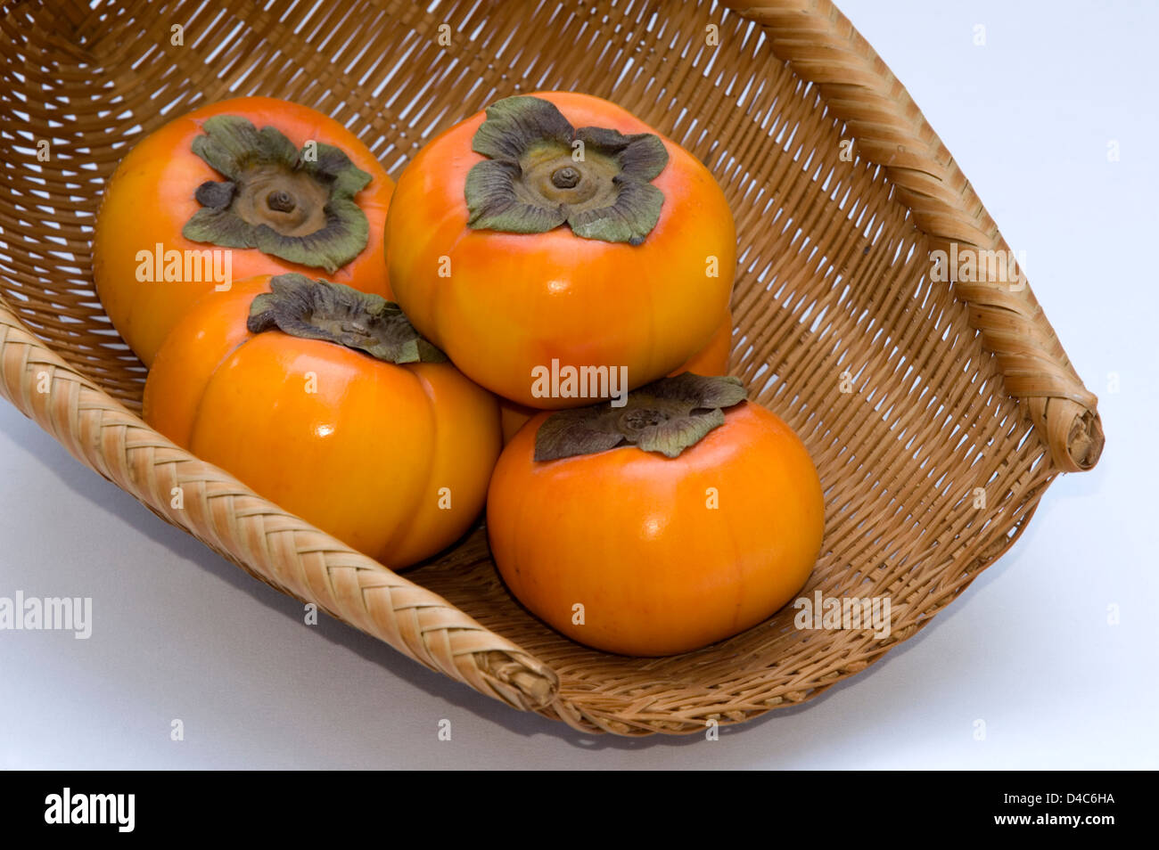 A wicker basket containing fresh Japanese 'kaki' persimmon fruit. Stock Photo