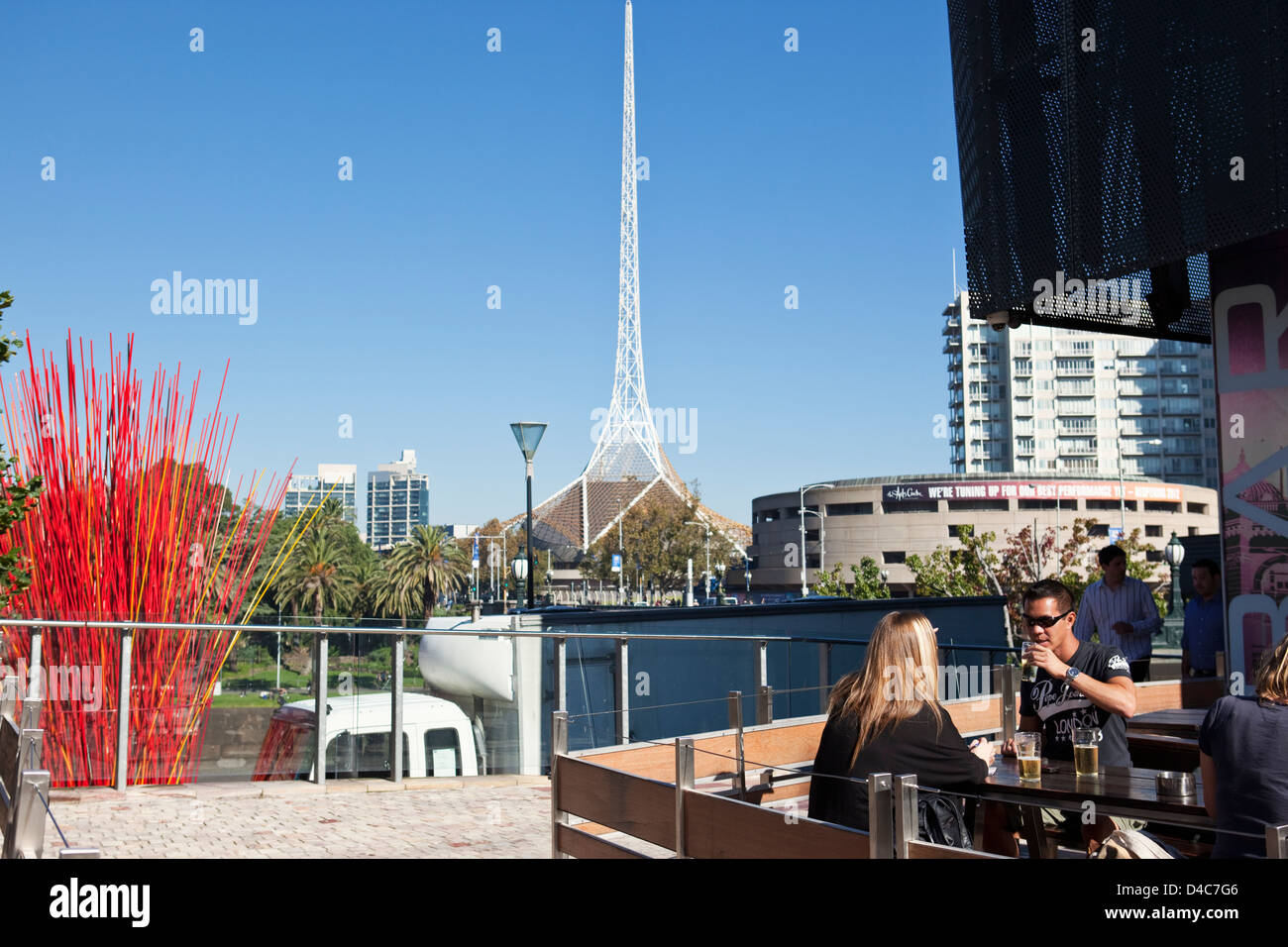 People relaxing at bar in Federation Square with spire of Victorian Arts Centre in background. Melbourne, Victoria, Australia Stock Photo