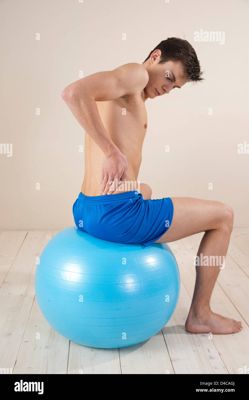 young man touching his back on a gymnastics ball Stock Photo
