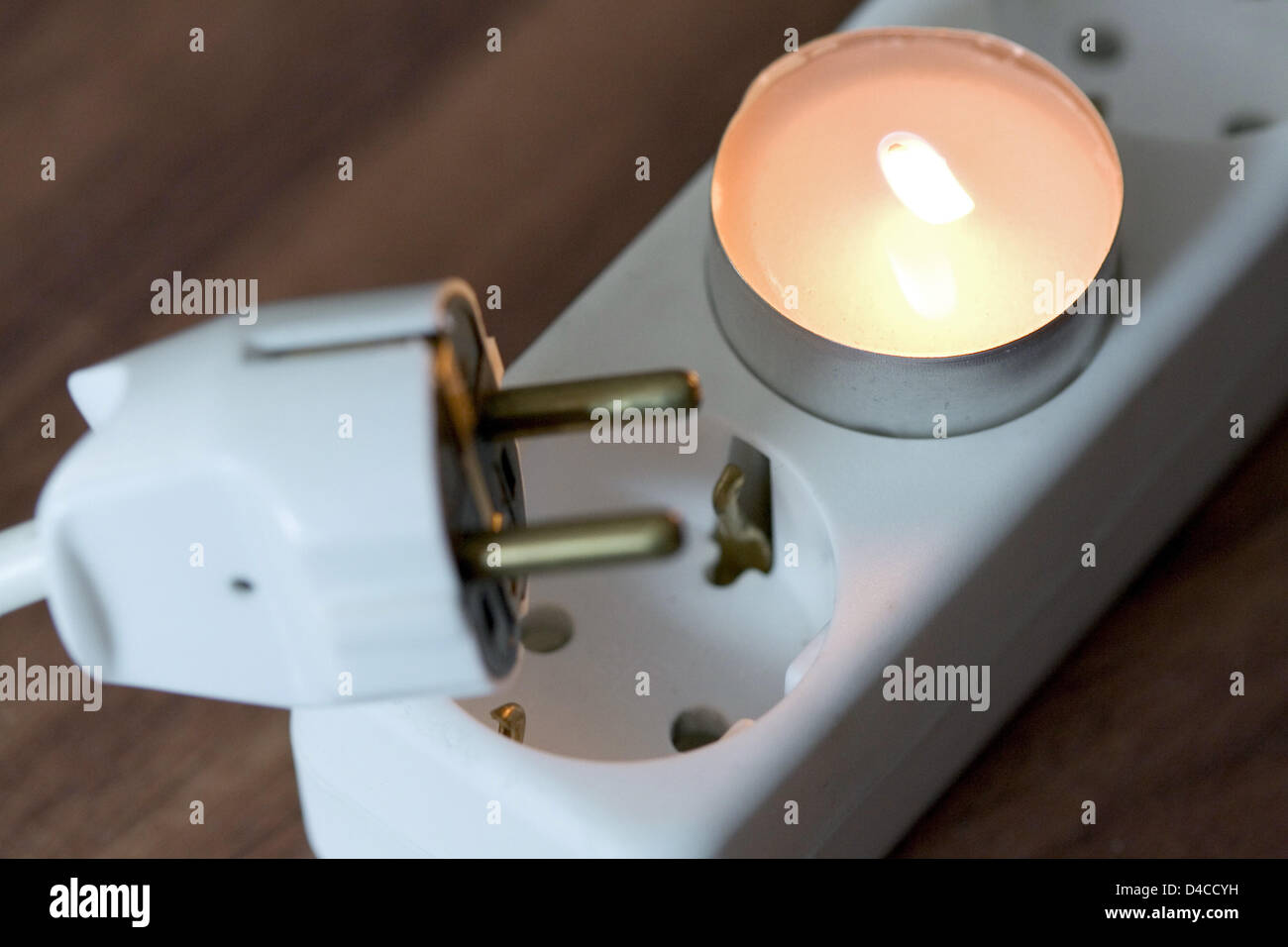 A lit tealight is placed in a power socket next to a plug and another socket in Osnabrueck, Germany, 14 January 2008. Illustration on the topic: Energy, electricity, additional costs. Photo: Friso Gentsch Stock Photo