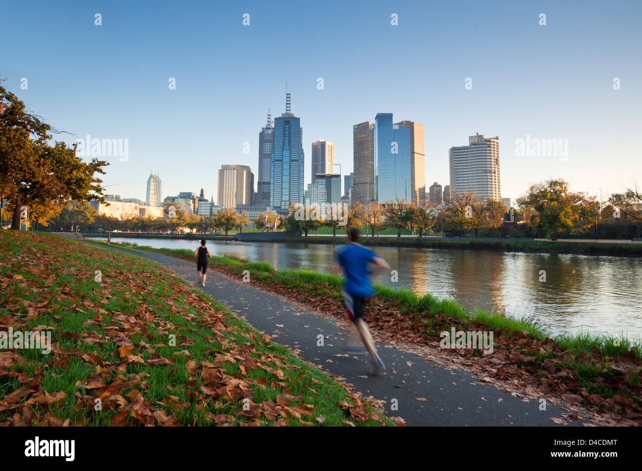 Joggers on banks of Yarra River with city skyline in background. Melbourne, Victoria, Australia Stock Photo