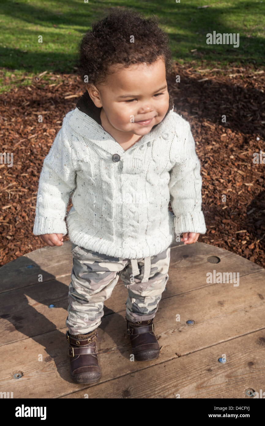 mixed race toddler standing on wooden platform wearing cream jumper and