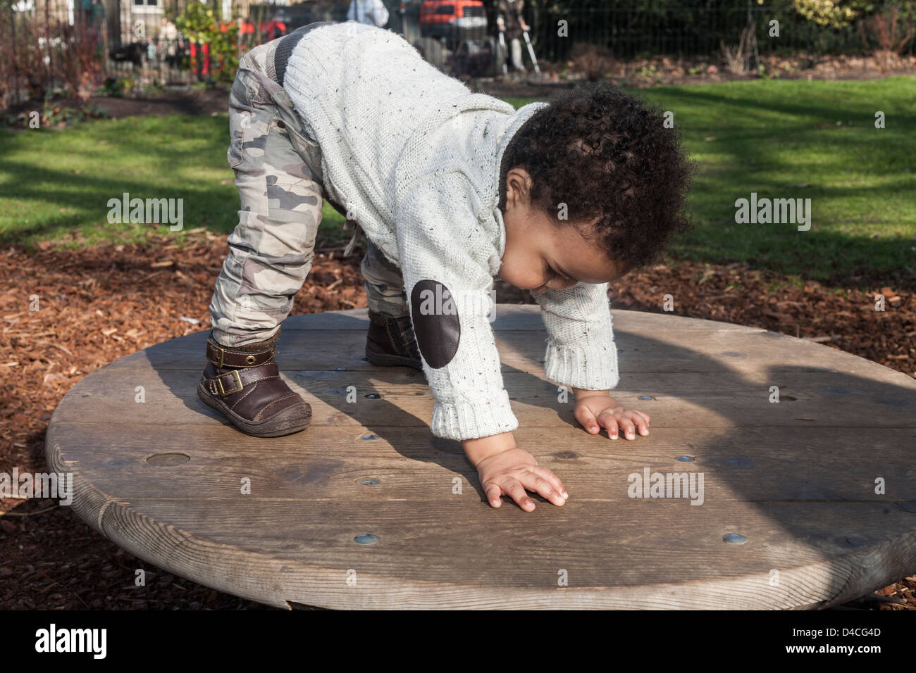 mixed race toddler on wooden platform wearing cream jumper and combats doing yoga in the sunshine Stock Photo