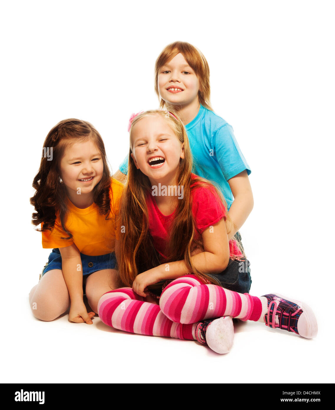 Group of three kids, two girls and boy together, diversity looking happy, laughing, hugging, sitting on the floor isolated on white Stock Photo
