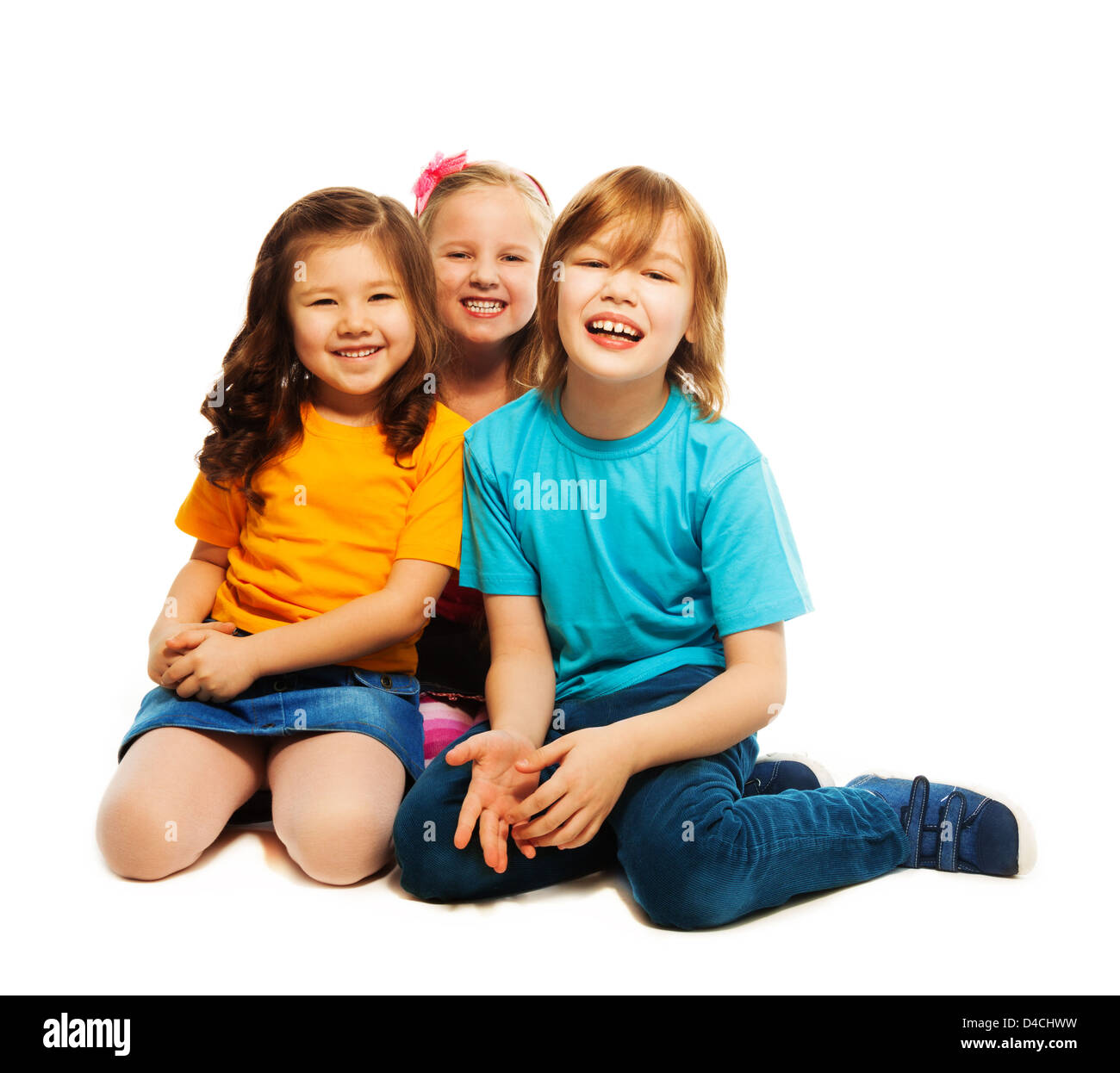 Group of three happy hugging kids, two girls and boy together, diversity looking, laughing, sitting on the floor isolated on white Stock Photo