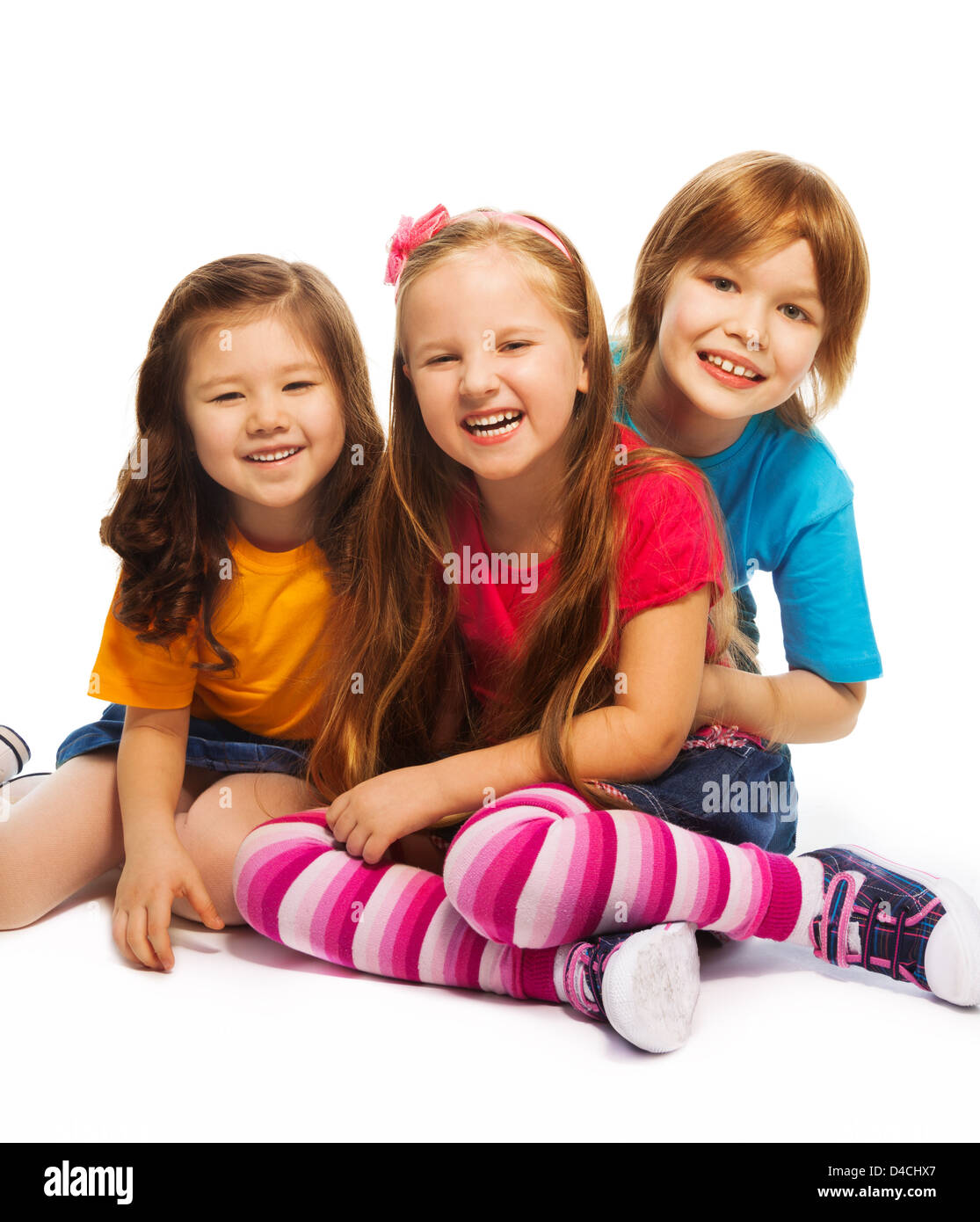 Group of three kids, two girls and boy together, happy, laughing, hugging, sitting on the floor isolated on white Stock Photo