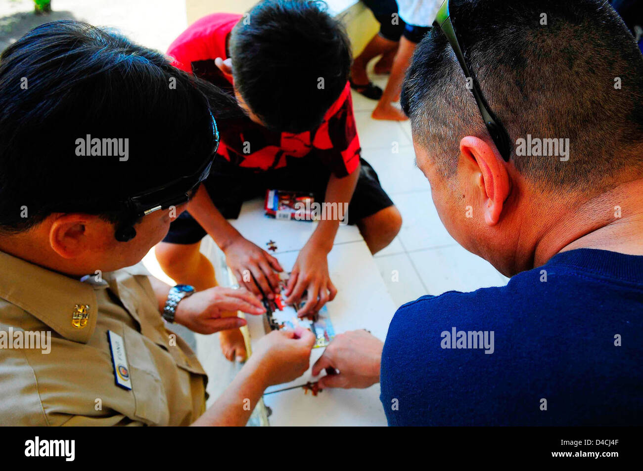 Command Master Chief, Master Chief Hospital Corpsman (SW/FMF) Noel Manlapaz and Master Chief Culinary Specialist (SW/AW) Jack Fong Piece Together a Puzzle With an Indonesian Boy Stock Photo