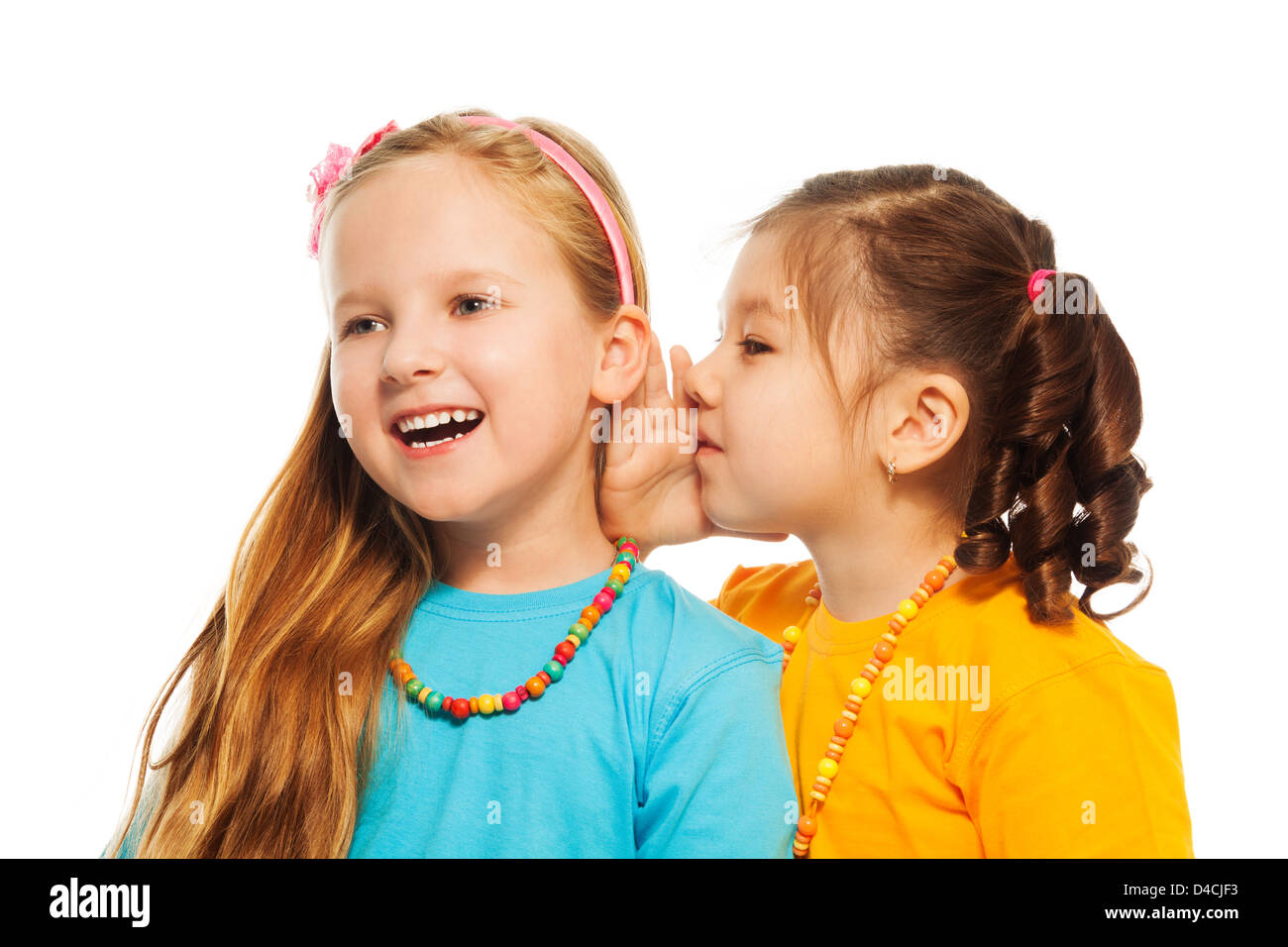 Two little 6-7 years old Asian and Caucasian girls with pile of books gossip about something funny smiling and laughing, isolated on white Stock Photo