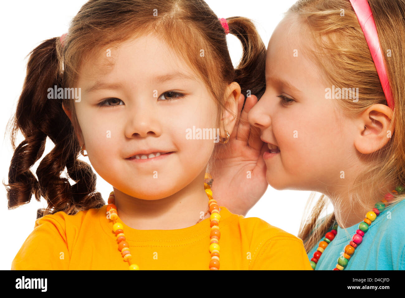 Closeup of two little 6-7 years old Asian and Caucasian girls gossip telling secrets mouse to ear, isolated on white Stock Photo