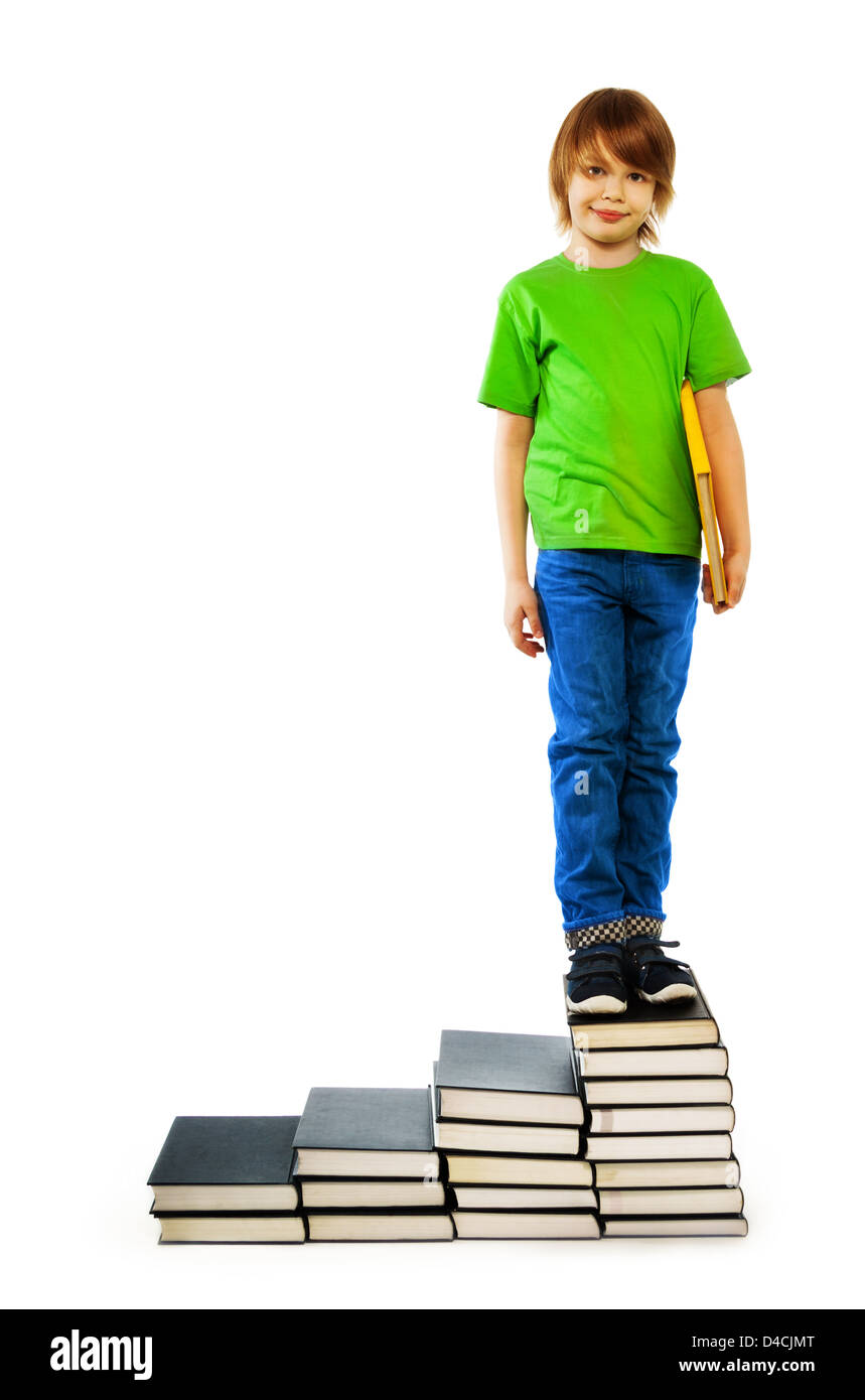 Happy Caucasian 9 years old boy in green shirt sitting on stairs made of stack of books, isolated on white Stock Photo