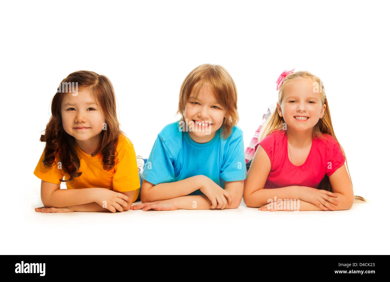 Three happy kids, boy and two girls laying on the floor in a line together smiling and laughing, isolated on white Stock Photo