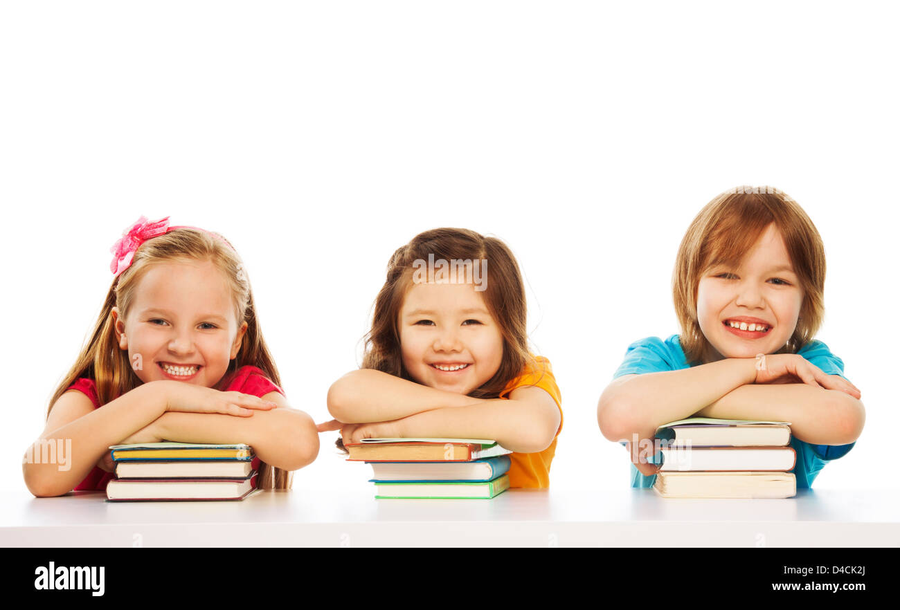 Three kids boy and girls laying on pile of books on the table, smiling, laughing, isolated on white Stock Photo