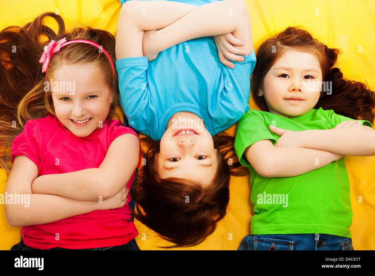 Three little kids, boys and girls, laying on the yellow mattress, smiling, with long hair, Stock Photo