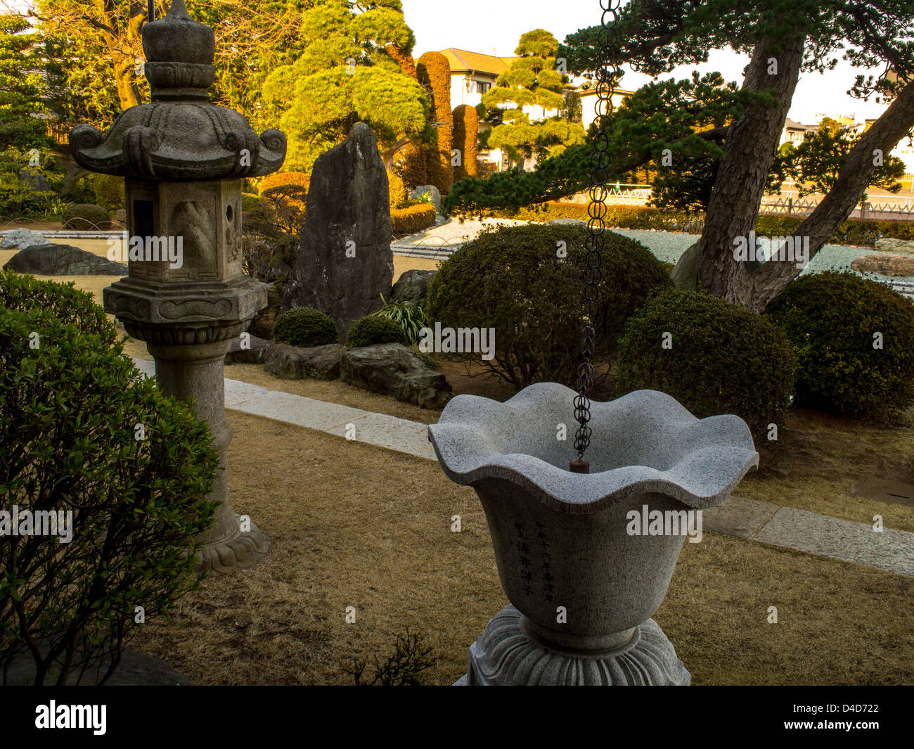A stone lantern and rain water cistern with late afternoon sunshine on the trees beyond,  in a Japanese temple garden. Stock Photo