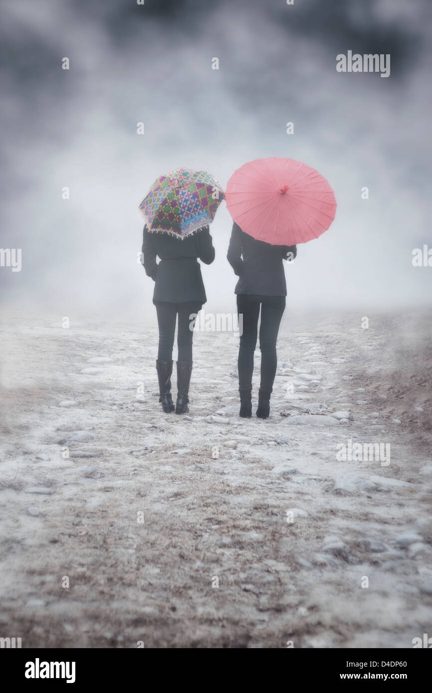 two girls with colourful umbrellas are walking in the mist Stock Photo
