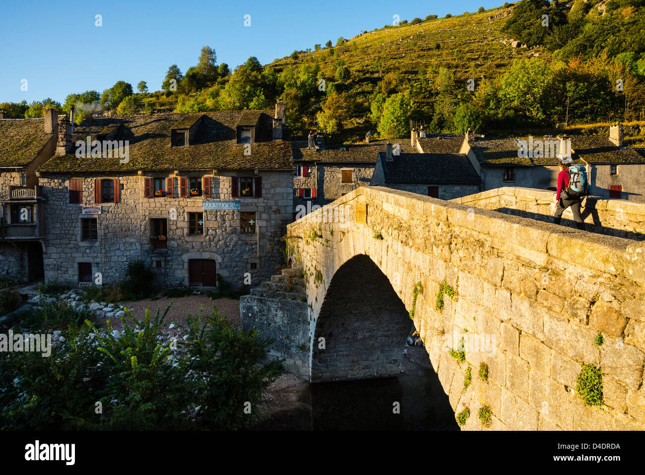 Walker in evening sunlight crossing the bridge at le Pont de Montvert on the Robert Louis Stevenson Trail Lozère, France Stock Photo